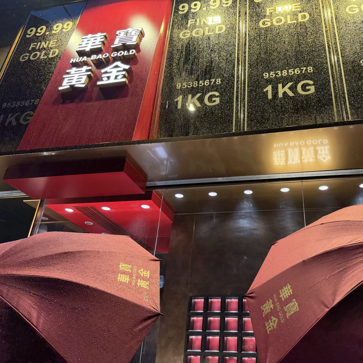 雨中的華寶黃金招牌，前方是印有品牌名稱的紅色雨傘